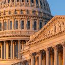 Close-up of the U.S. Capitol dome and an ornate portico illuminated by warm sunlight against a blue sky.