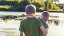 Two boys stand in front of a pond.