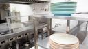 A stock image of plates stacked on a stainless steel shelf in a kitchen.