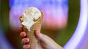 A hand holds a waffle cone with ice cream scoops