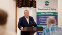 Pennsylvania Department of Aging Secretary Jason Kavulich speaks at a podium during an event, with a banner behind him outlining the department's mission to support older adults.