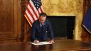 Governor Josh Shapiro signs an executive order at a wooden desk, with an American flag in the background on August 18, 2026.