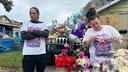 A man and woman stand at a memorial of flowers, balloons, and candles.