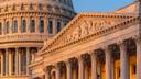 Close-up of the U.S. Capitol dome and an ornate portico illuminated by warm sunlight against a blue sky.