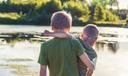 Two boys stand in front of a pond.