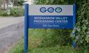 A blue sign that says “Geo Moshannon Valley Processing Center” in front of green leaves.