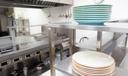 A stock image of plates stacked on a stainless steel shelf in a kitchen.