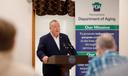 Pennsylvania Department of Aging Secretary Jason Kavulich speaks at a podium during an event, with a banner behind him outlining the department's mission to support older adults.