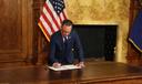 Governor Josh Shapiro signs an executive order at a wooden desk, with an American flag in the background on August 18, 2026.