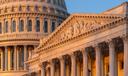 Close-up of the U.S. Capitol dome and an ornate portico illuminated by warm sunlight against a blue sky.