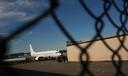 An airplane and a building seen through a chain link fence.