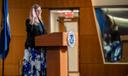 Jennifer Higgins, then-USCIS deputy director, swears in new citizens while raising her hand at a podium with the USCIS seal.