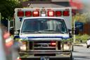 An ambulance seen head on with its lights on in the daylight.
