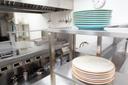 A stock image of plates stacked on a stainless steel shelf in a kitchen.