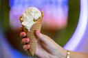 A hand holds a waffle cone with ice cream scoops