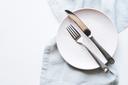 A stock image of an empty plate and cutlery on a white table.