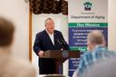 Pennsylvania Department of Aging Secretary Jason Kavulich speaks at a podium during an event, with a banner behind him outlining the department's mission to support older adults.