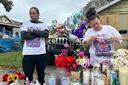 A man and woman stand at a memorial of flowers, balloons, and candles.