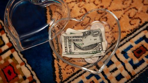 A couple of dollars and some change once belonging to James Pschirer sit in a heart-shaped glass container as photographed Thursday, Feb. 25, 2021.