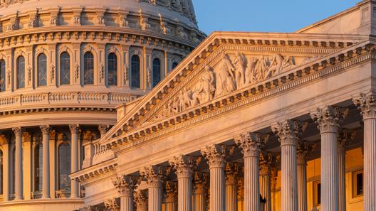 Close-up of the U.S. Capitol dome and an ornate portico illuminated by warm sunlight against a blue sky.