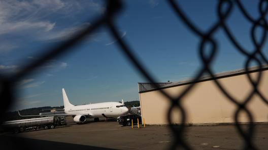 An airplane and a building seen through a chain link fence.