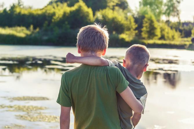 Two boys stand in front of a pond.