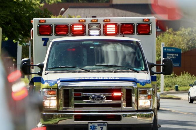 An ambulance seen head on with its lights on in the daylight.