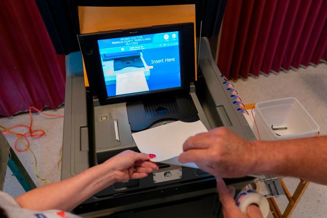 A polling judge helps guide a voter's ballot into a voting machine during the May 2022 Pennsylvania primary election.