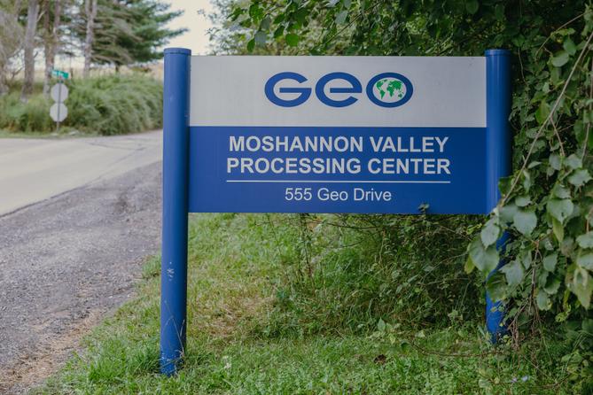 A blue sign that says “Geo Moshannon Valley Processing Center” in front of green leaves. A blue sign that says “Geo Moshannon Valley Processing Center” in front of green leaves.