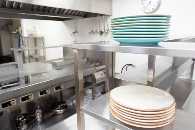 A stock image of plates stacked on a stainless steel shelf in a kitchen. A stock image of plates stacked on a stainless steel shelf in a kitchen.