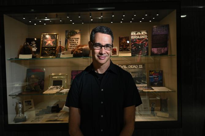 Adam Lowenstein stands in front of a display case of horror artifacts.