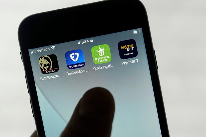 FanDuel, DraftKings, and other online gambling apps are displayed on a phone.