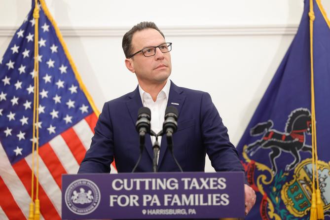 Gov. Josh Shapiro at a podium surrounded by flags.