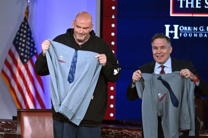Democratic Sen. John Fetterman (left) and Republican Sen. Dave McCormick of Pennsylvania display hoodies presented by the Edward M. Kennedy Institute for the United States Senate after participating in a debate Monday, June 2, 2025 in Boston.