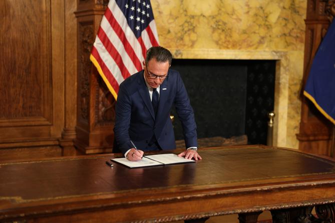 Governor Josh Shapiro signs an executive order at a wooden desk, with an American flag in the background on August 18, 2026. Governor Josh Shapiro signs an executive order at a wooden desk, with an American flag in the background on August 18, 2026.