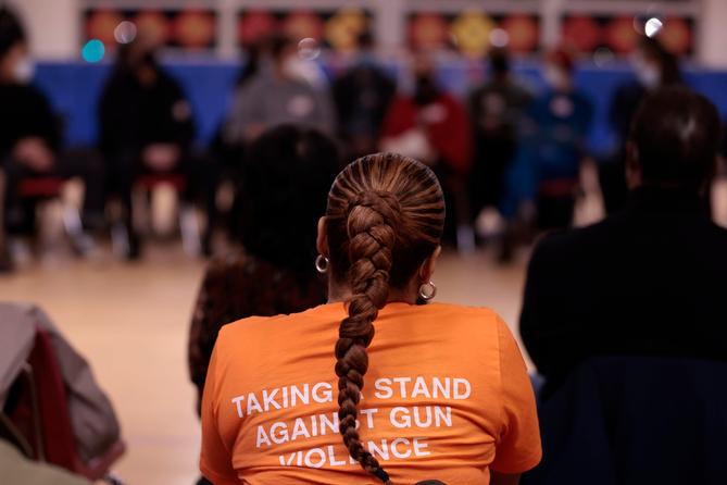 A student with long hair in a braid wears an orange T-shirt that says "taking a stand against gun violence."