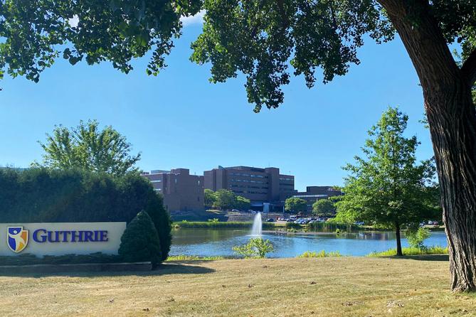 A health system campus framed by trees with a sign that says “Guthrie.”
